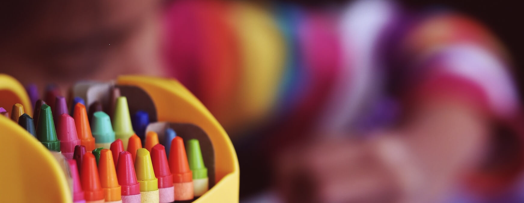 the image shows crayons and a child colouring in the background which represents our free creative support services for children impacted by mental health needs.