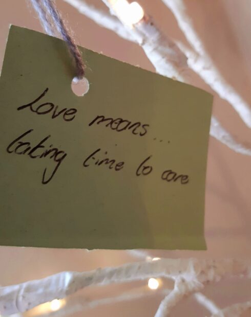 A hand written tag on a lit tree, saying 'Love means taking time to care'