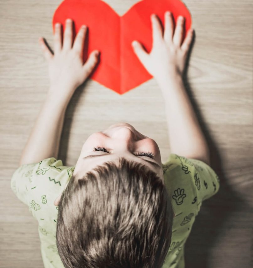 A child holds a cut out love heart reflecting our services for children with SEMH needs delivered with love, imagination and creativity.